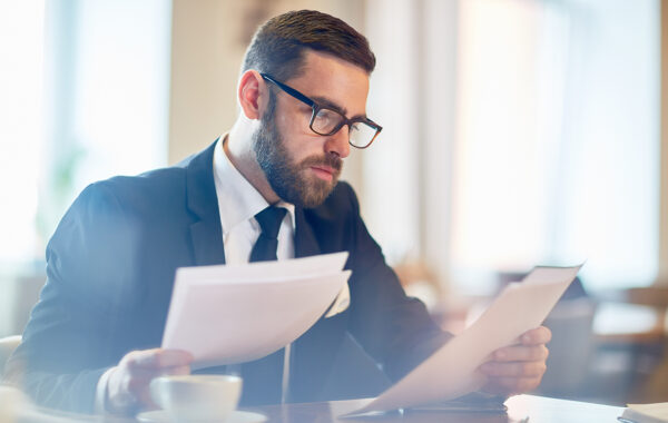 Confident banker reading financial papers while sitting in cafe